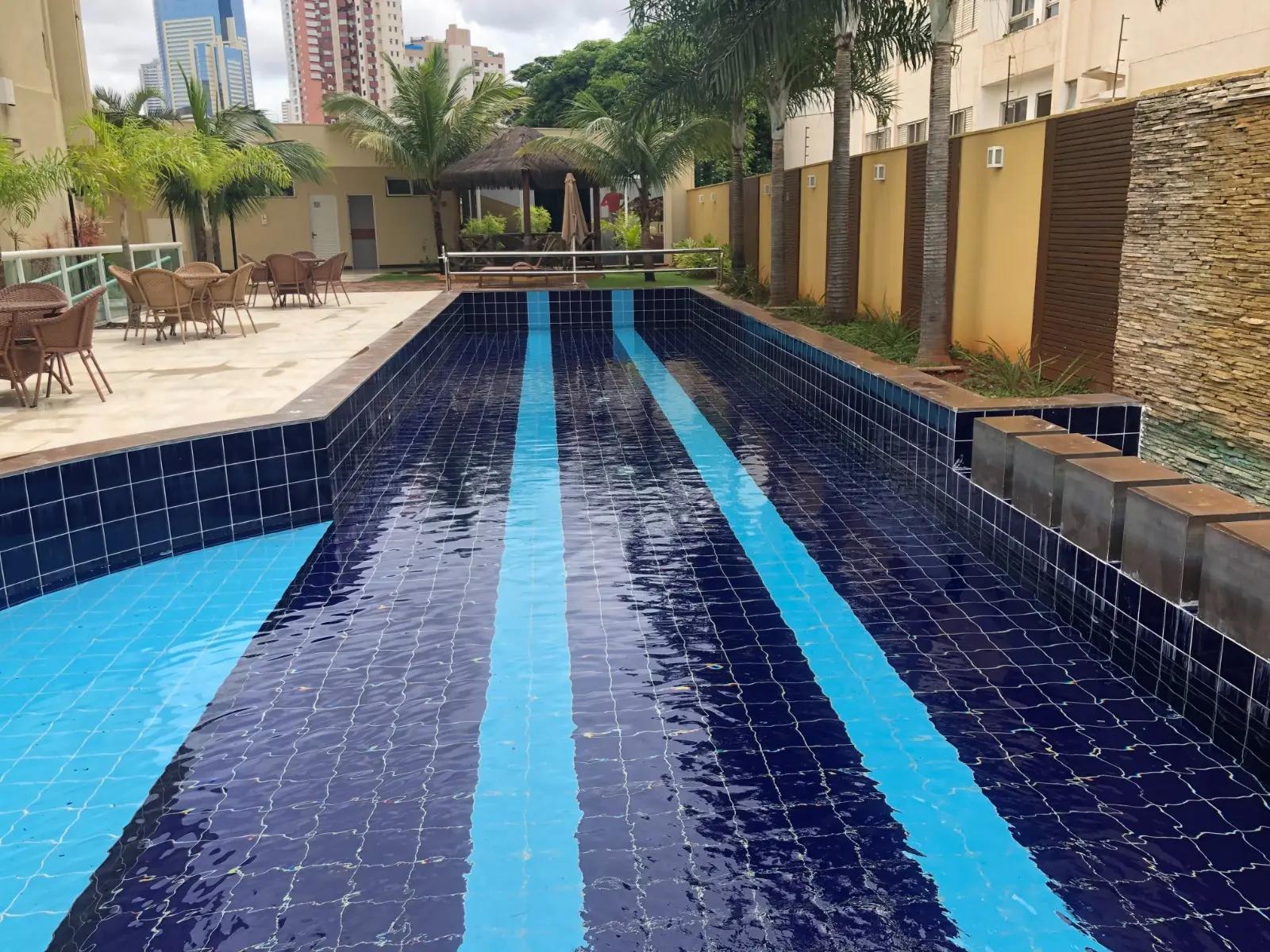 Piscina de raias com revestimento em pastilhas e deck em condomínio em Goiânia